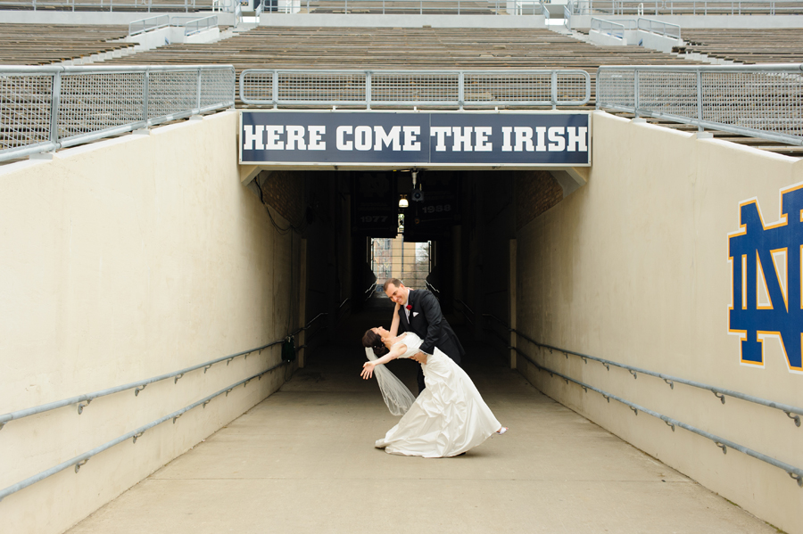 elegant bride and groom dipping under here come the irish sign on the notre dame football field