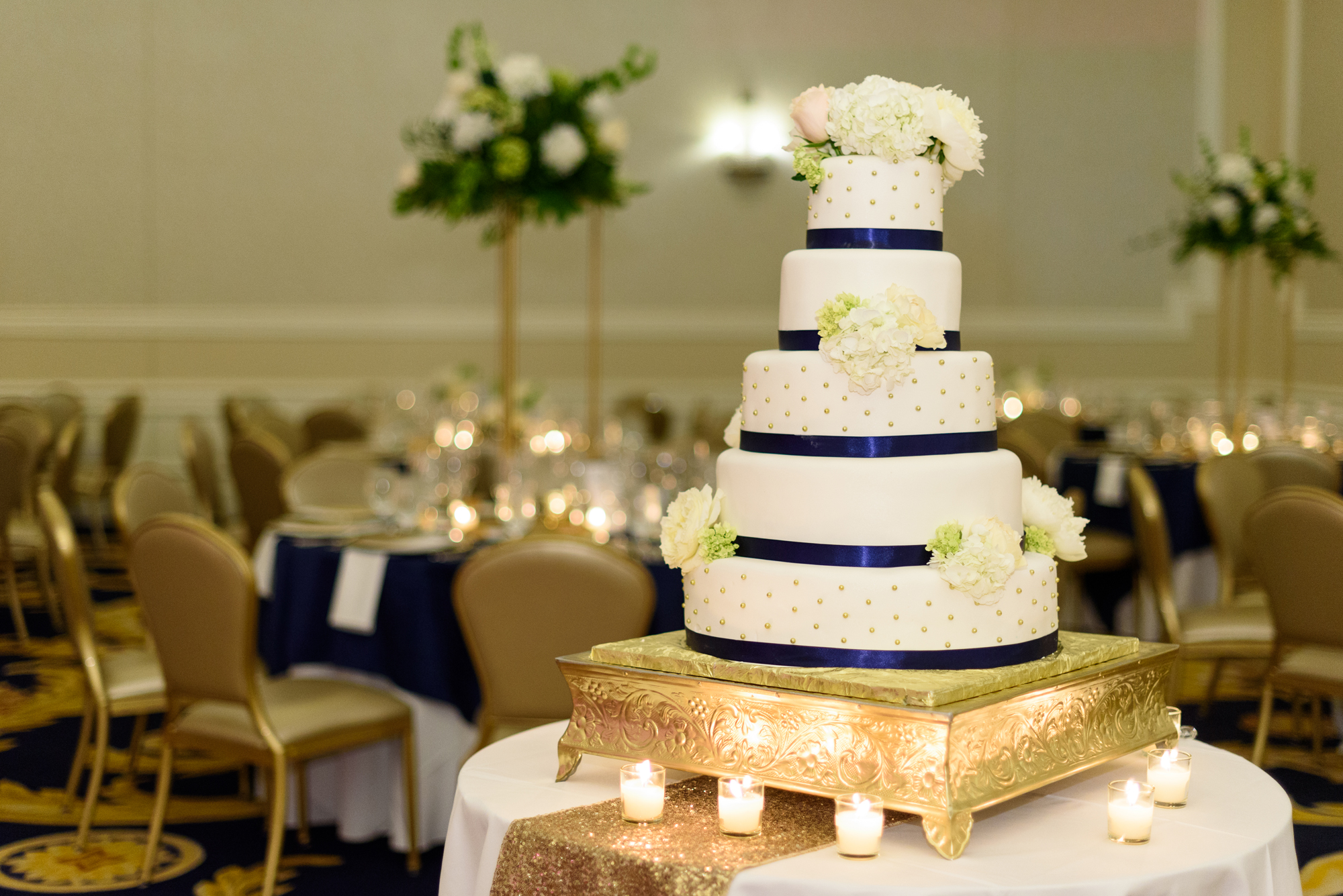 Timeless wedding cake with navy blue ribbon with a gold stand.