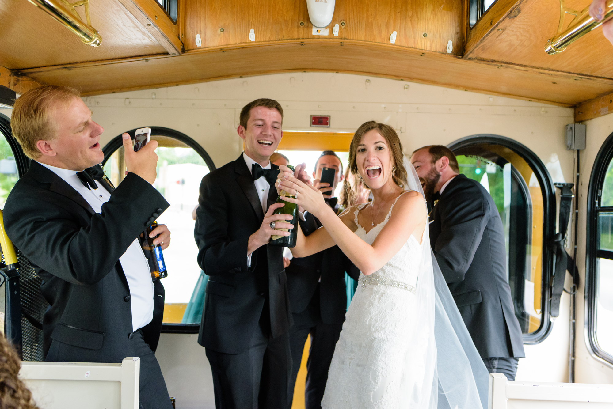 bride & groom on the way to the reception in a trolley opening champaign with their bridal party