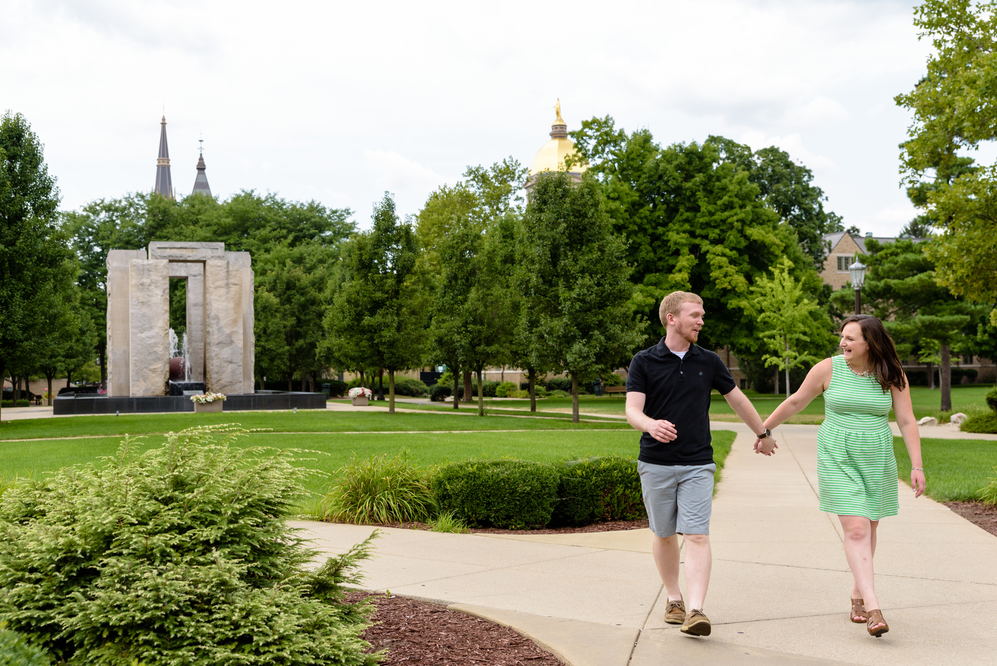 Engaged couple at the Clarke Memorial Fountain with the Basilica and Dome in the background on the campus of the University of Notre Dame